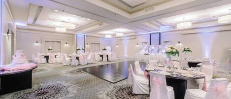 Un amplio salón de banquetes con mesas redondas, sillas blancas y centros de mesa florales.