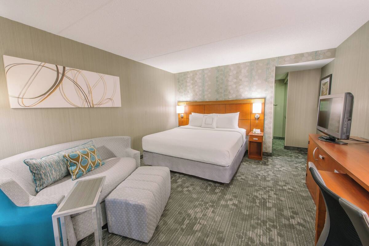 A hotel room with a bed, a sofa, a desk, and a television.