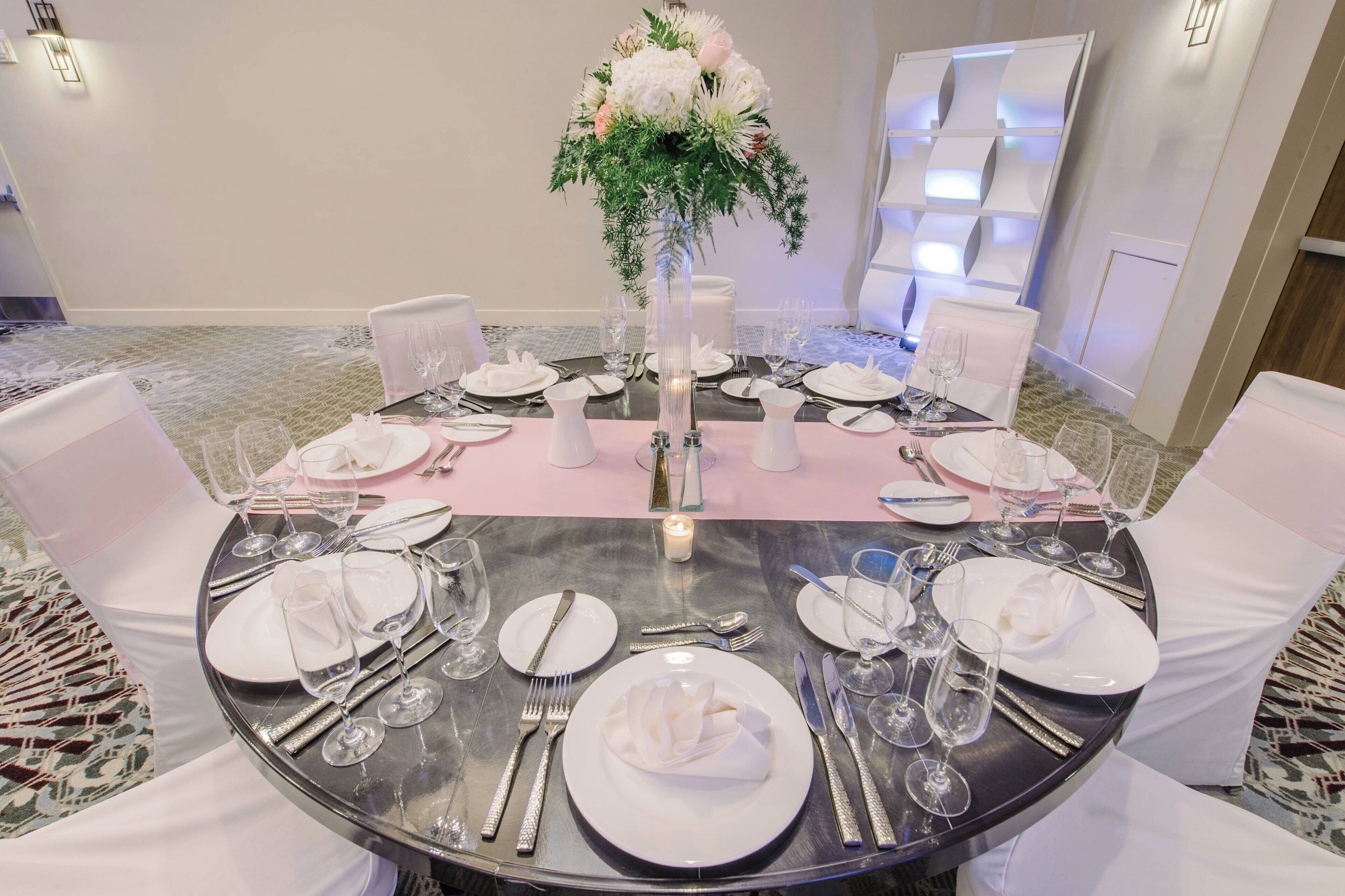 Une table ronde dressée pour un événement formel, avec des nappes blanches, des couverts en argent et de la verrerie élégante.