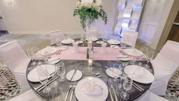A round dining table set for a formal event with white tablecloths, silverware, and glassware.