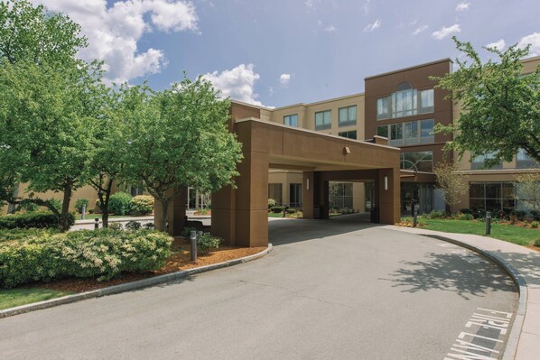 A modern building with a covered entrance, landscaped gardens, and a clear sky.