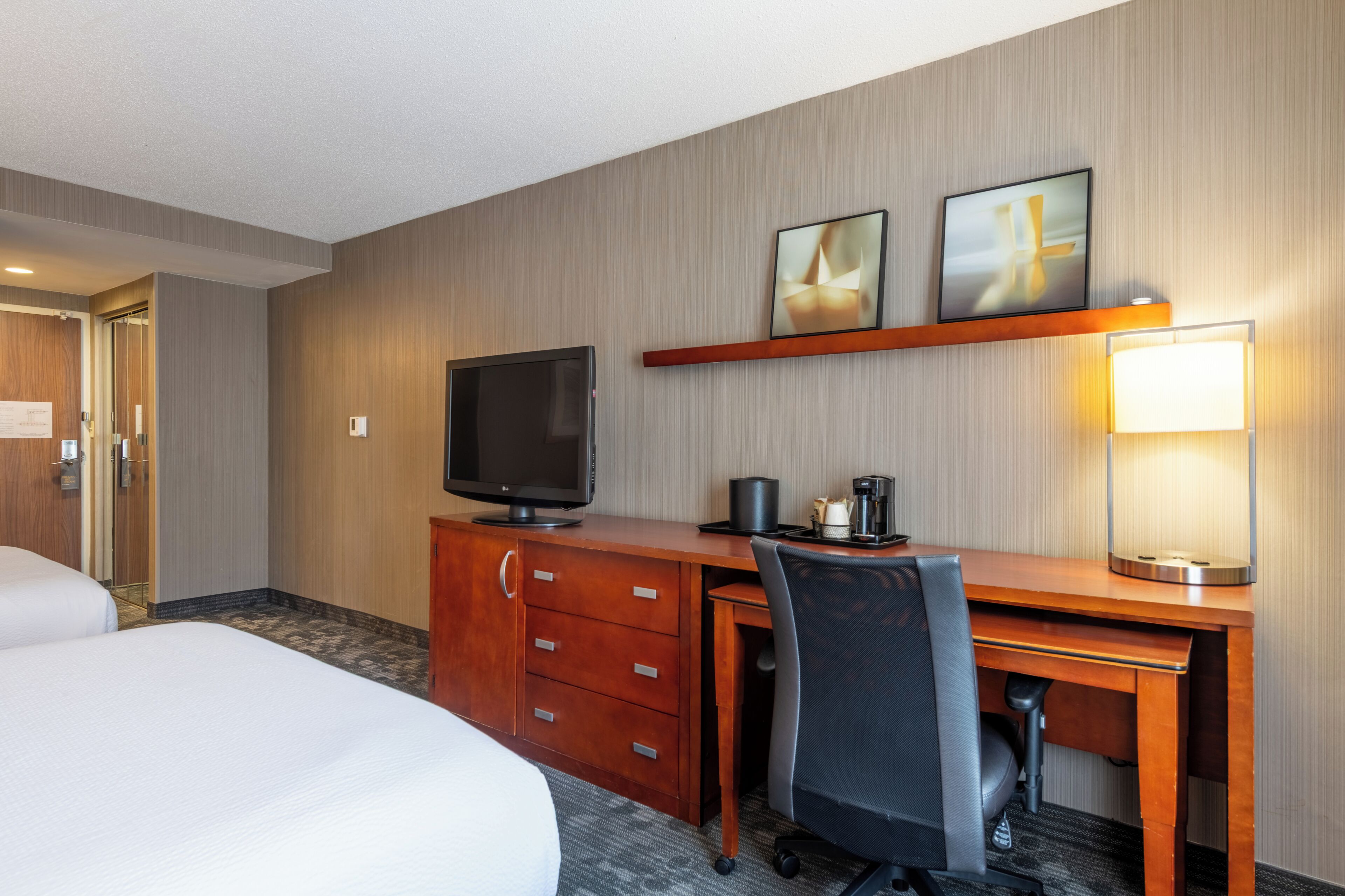 Ein Hotelzimmer mit zwei Betten, einem Schreibtisch, einem Computer, einem Fernseher und einer Lampe.