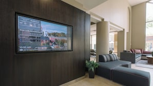 A modern hotel lobby with a large digital display showing local news, a comfortable seating area, and a view of the city. - Courtyard by Marriott Nashua (Nashua)