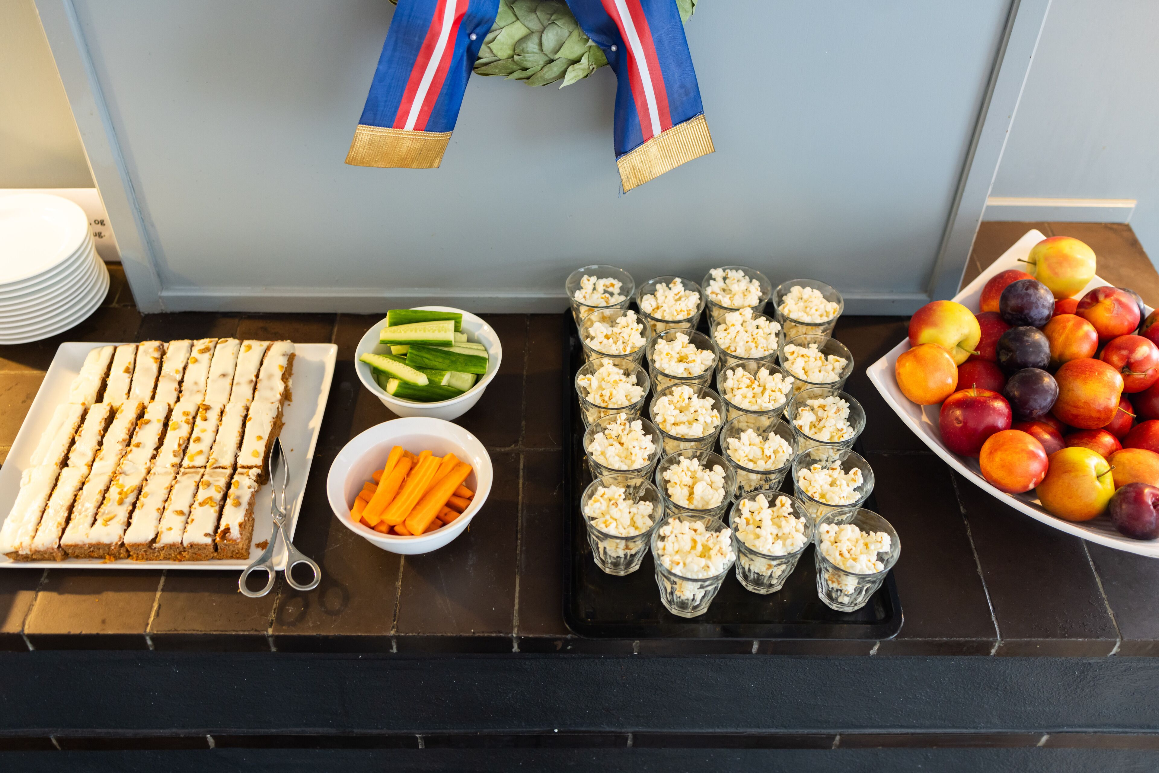 Une table de buffet avec des sandwichs coupés en tranches, des fruits et de petits verres de pop-corn.