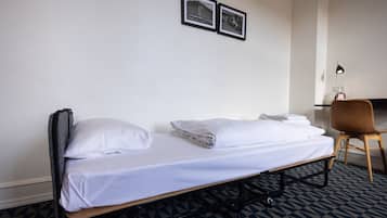 Ein Einzelbett mit weißer Bettwäsche, ein Sessel und zwei gerahmte Bilder an der Wand.