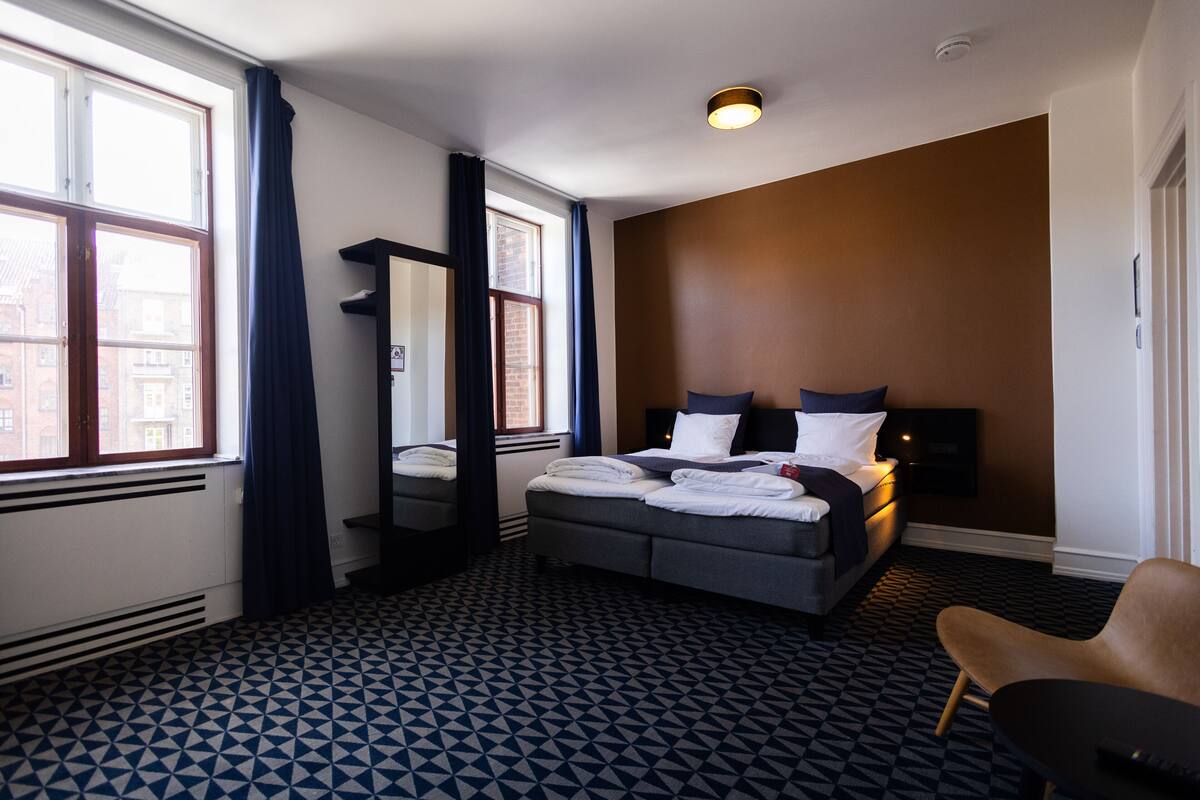 Een hotelkamer met een groot bed, een stoel, een bureau en een raam met gordijnen.