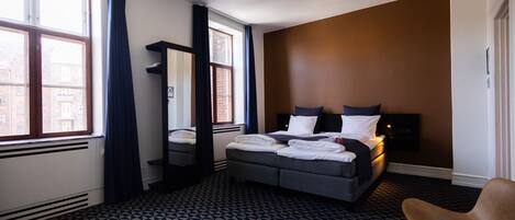A hotel room with a large bed, a chair, a desk, and a window with curtains.