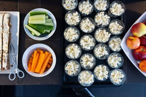A table with food items including sliced cucumbers, carrots, popcorn in glasses, and apples.