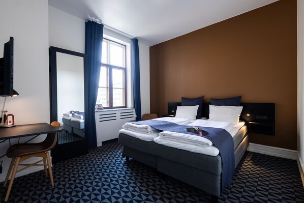 Habitación de hotel con cama, escritorio, silla, espejo y ventana con cortinas.