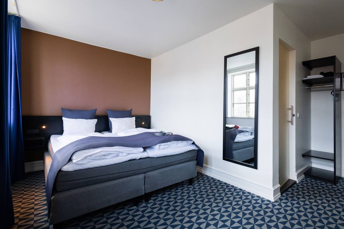 Een hotelkamer met een bed, een grote spiegel, een kledingkast en een vloer met een geometrisch patroon.