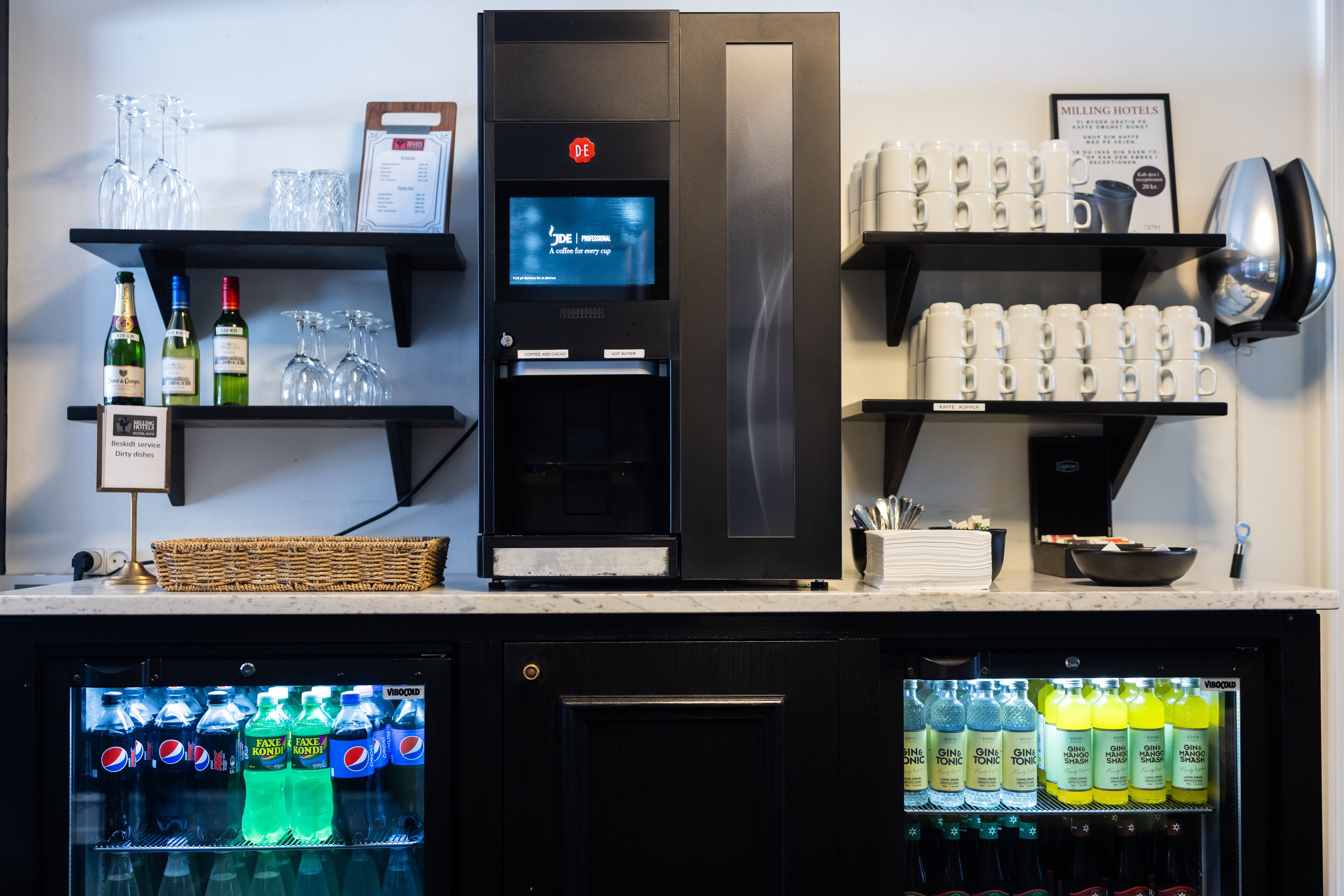 Un minibar con refrigerador, máquina de café y estantes con vasos y botellas.