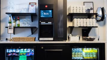 Un minibar con refrigerador, máquina de café y estantes con vasos y botellas.