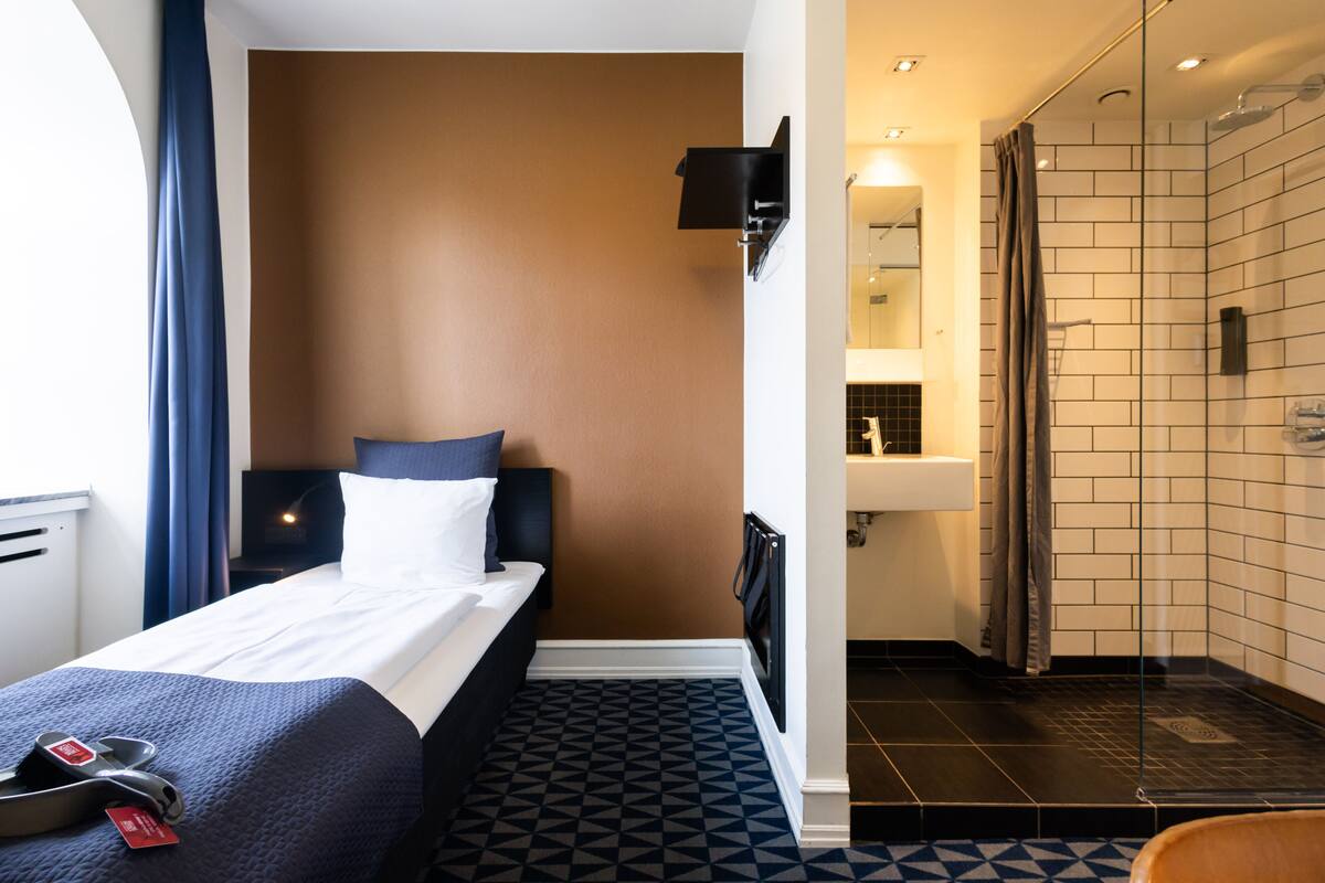Een hotelkamer met een bed, een nachtkastje, een badkamer met douche en een kamer met een patroon vloer.