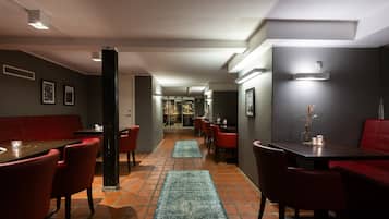 Un restaurante con cabinas y mesas rojas, piso de baldosas y una estantería de vinos visible al fondo.