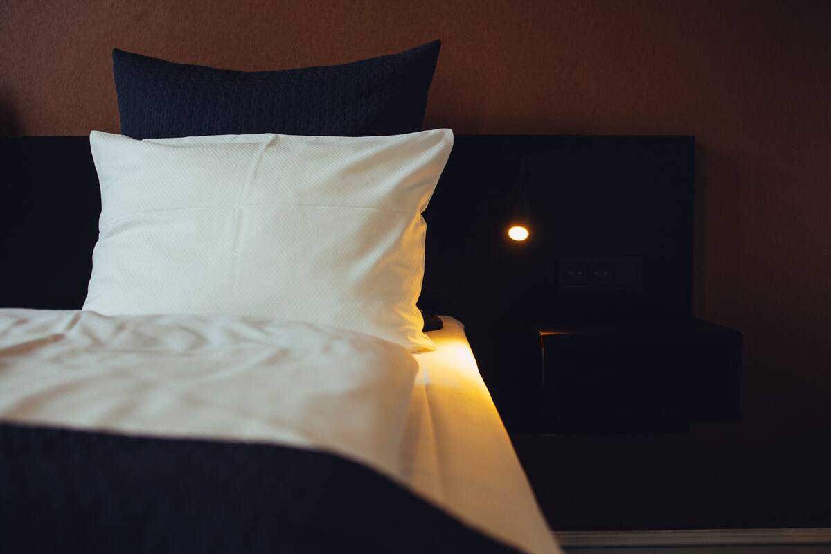 Een net opgemaakt bed met witte beddengoed en een donker hoofdbord.