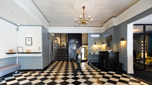 A hotel lobby with a checkered floor, a chandelier, a reception desk, and a staircase leading to the upper floors. - Milling Hotel Ritz (Aarhus)