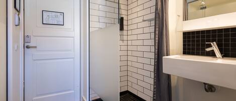 A bathroom with a white door, a shower with a glass partition, and a sink with a mirror above it.