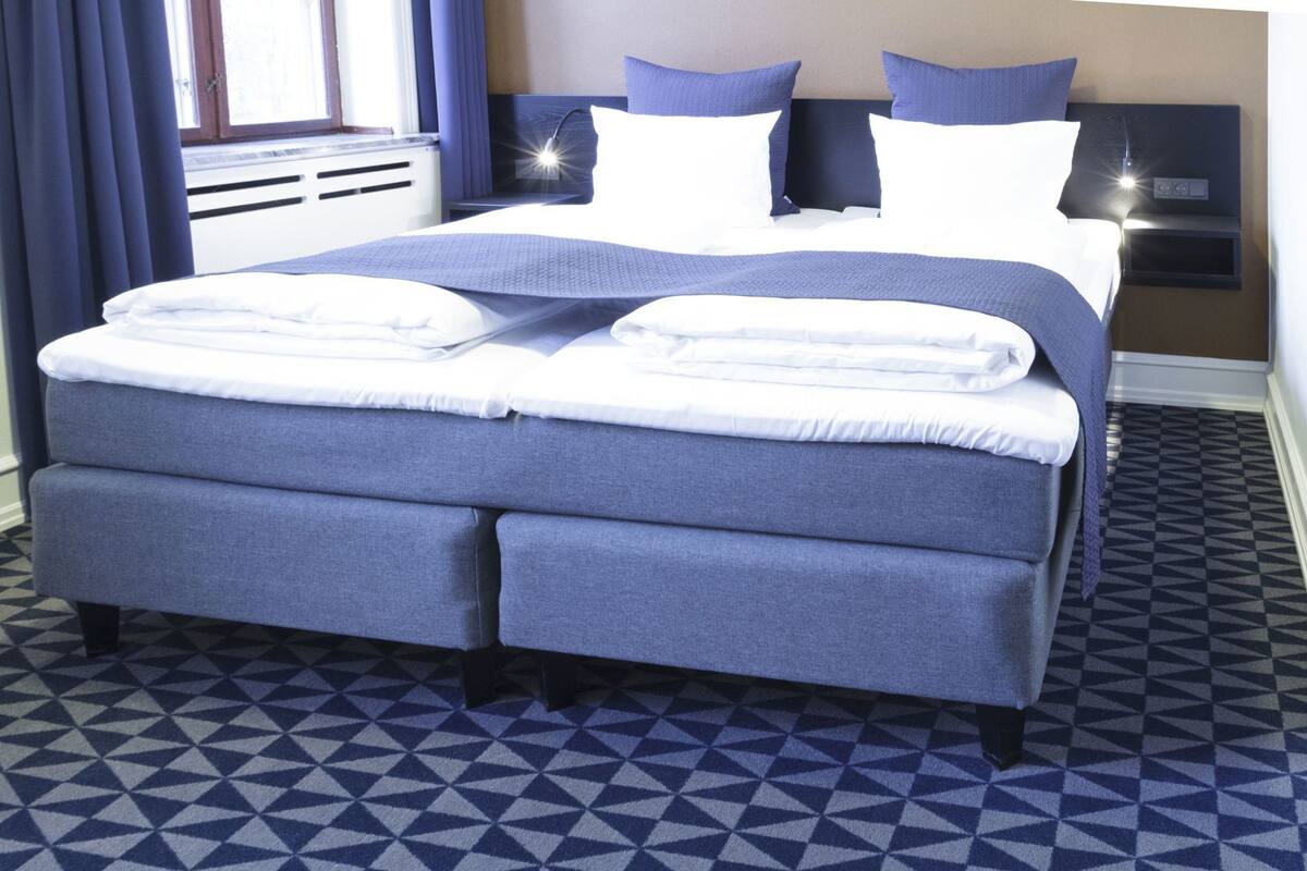 Een opgemaakt bed met een blauw-wit kleurenschema, een hoofdbord en een nachtkastje met een lamp.