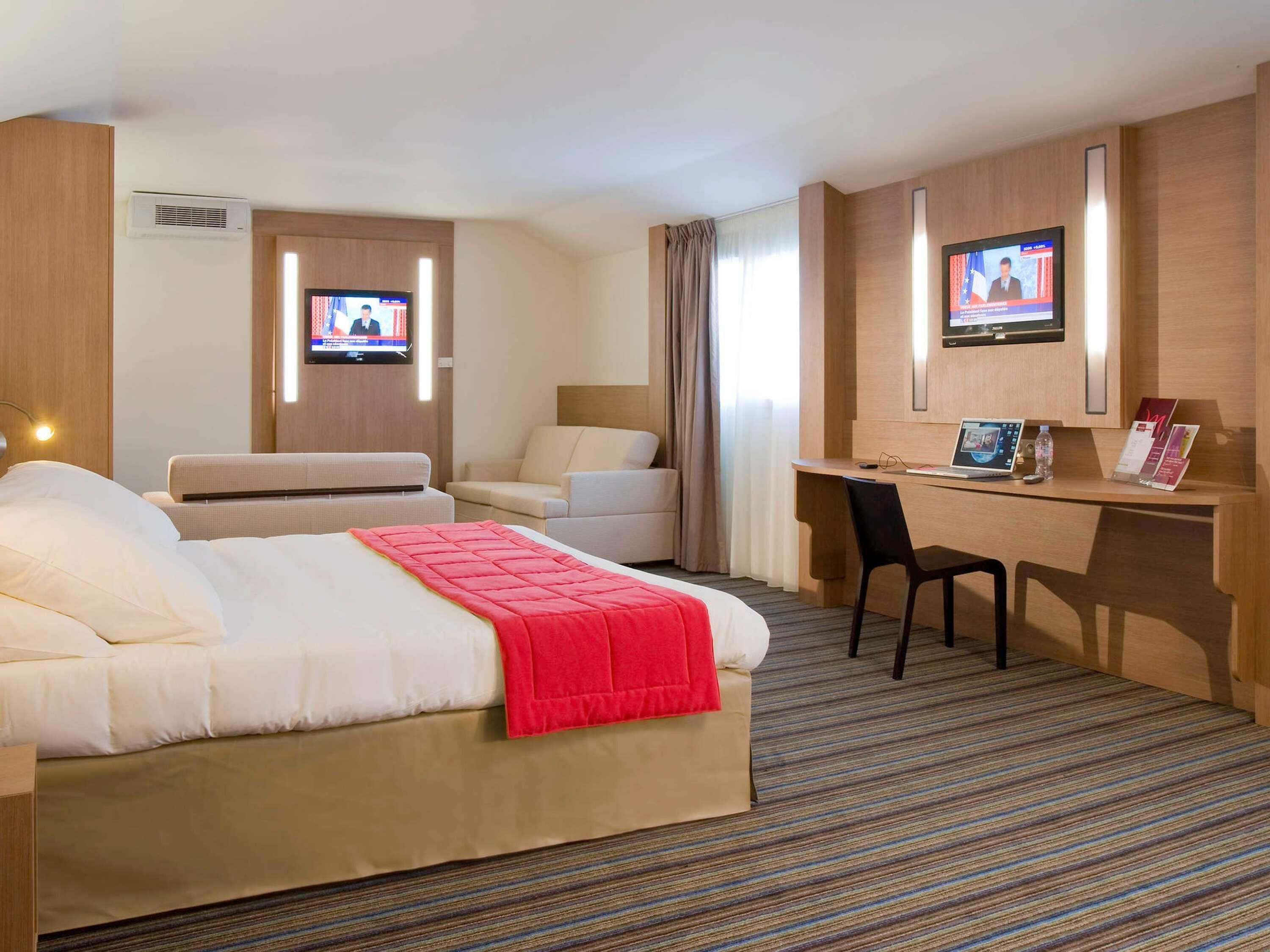 Habitación de hotel con cama, escritorio, dos sillas, televisor y aire acondicionado instalado en la pared.