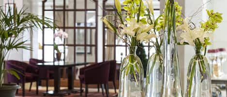 A dining area with a round glass table, several chairs, and a vase with flowers.