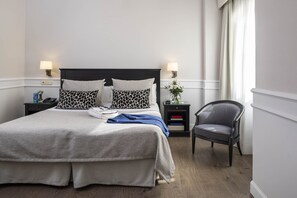 A neatly arranged hotel room with a large bed, two bedside tables with lamps, a chair, and a small table with a vase of flowers.