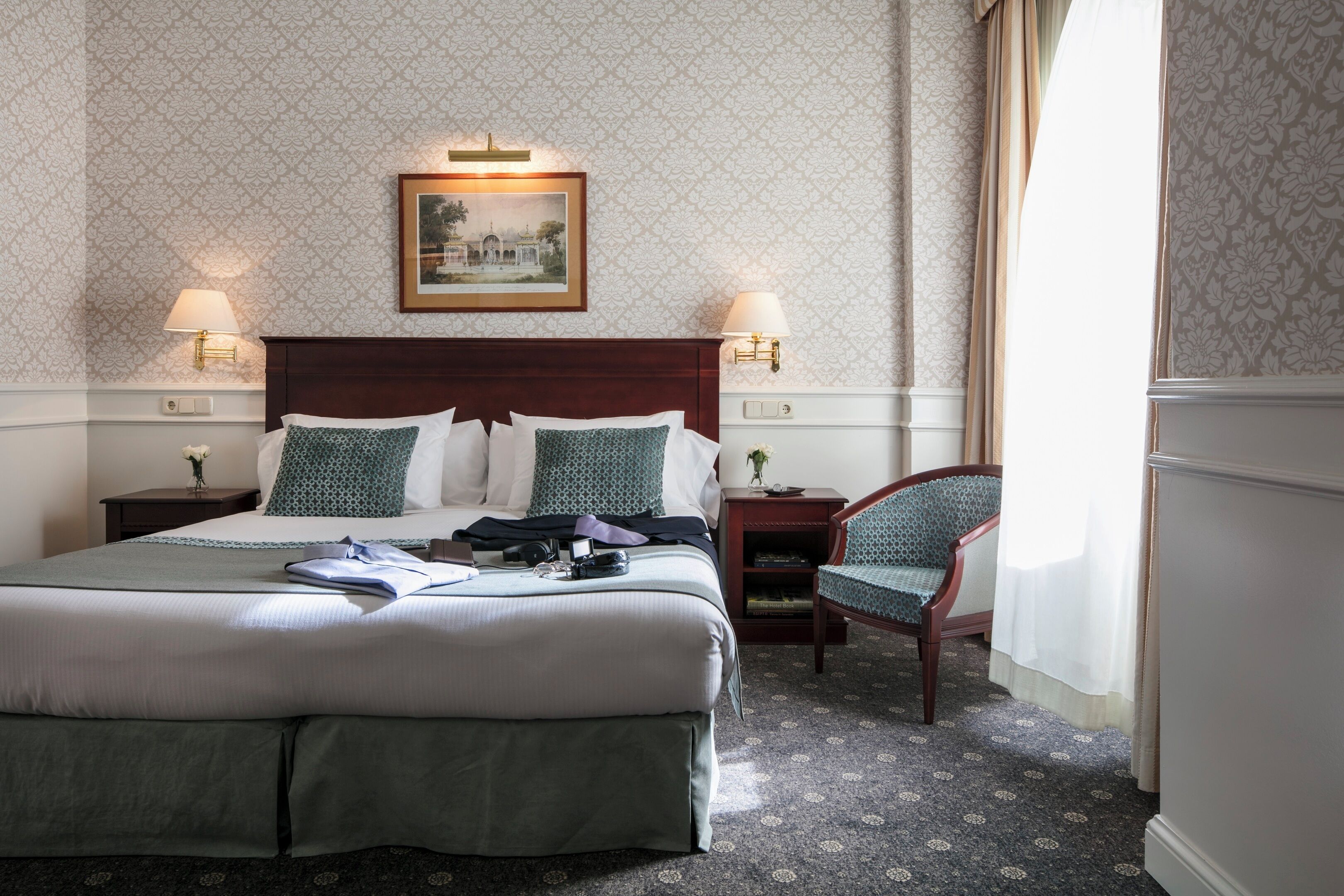 A hotel room with a large bed, two bedside tables with lamps, a chair, and a framed picture on the wall.