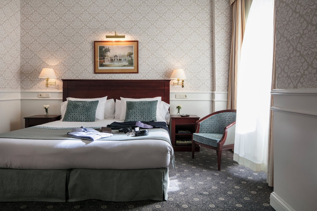 A hotel room with a large bed, two bedside tables with lamps, a chair, and a framed picture on the wall.