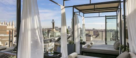 Una terraza en la azotea con vista a la ciudad, que incluye un sofá, una mesa con un jarrón y plantas en macetas.