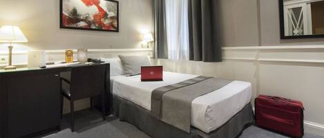 A hotel room with a bed, desk, laptop, and a red suitcase.