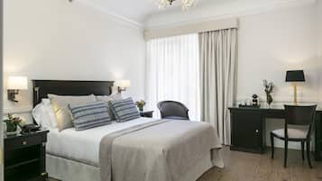 A hotel room with a large bed, two bedside tables with lamps, a desk with a chair, and a large window with curtains.