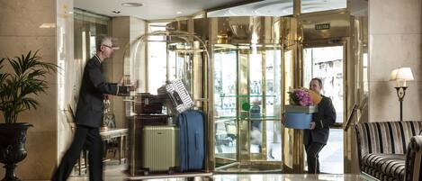 A hotel lobby with a reception desk, a luggage cart, and a sofa.