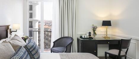 A hotel room with a bed, a desk, a chair, and a view of the city through the window.