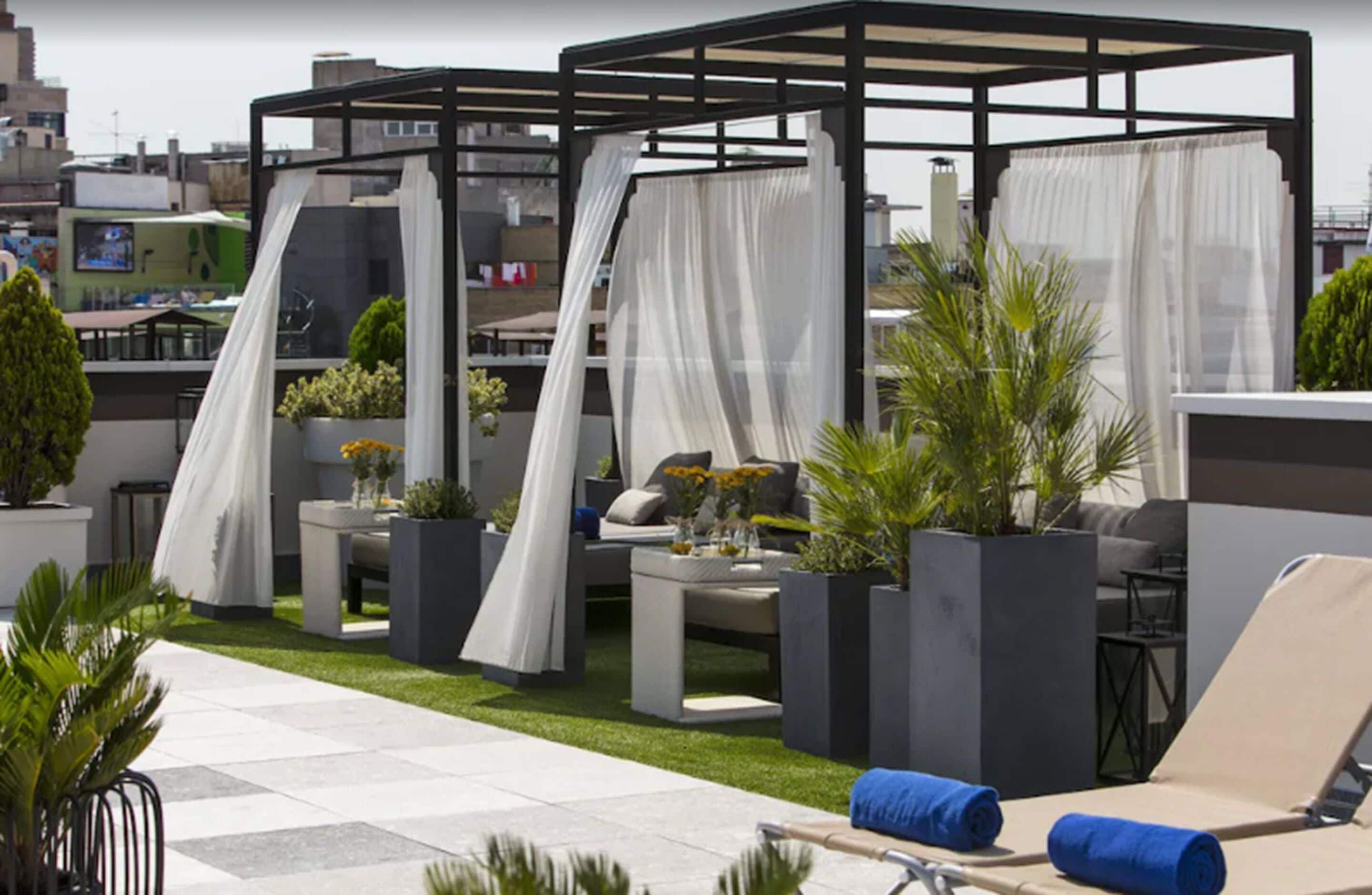Un área de lounge en la azotea con pérgola, asientos y plantas en macetas.