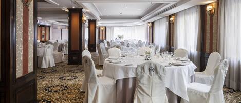 A banquet hall with round tables set for a formal event, featuring white tablecloths and matching chairs.