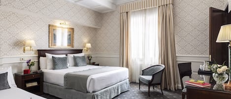 A hotel room with a large bed, two bedside tables, a desk, a chair, and a chandelier.
