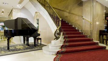 Un gran piano en un vestíbulo amplio con una escalera de mármol y peldaños alfombrados en rojo.