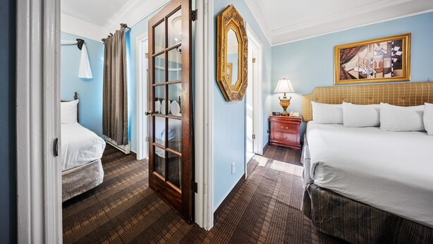 A hotel room with a large bed, a smaller bed, a wooden door, a mirror, and a painting on the wall. - Fitzgerald Hotel (San Francisco)