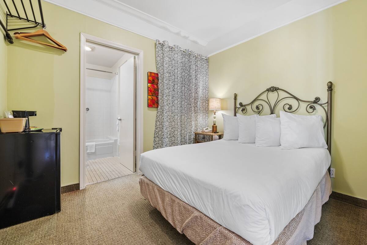 Un dormitorio con cama, mesita de noche, lámpara, perchero y una puerta que da a un baño.