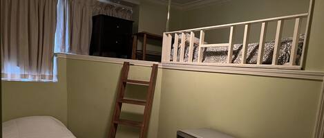 Una habitación con literas, una escalera, un microondas y una ventana con cortinas.