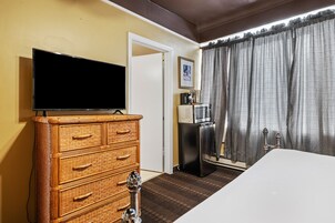 A hotel room with a television on a dresser, a minibar, a bed, and a window with curtains.