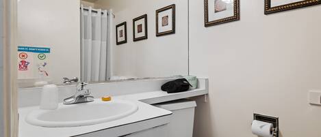 A bathroom with a white sink, a mirror, a toilet, and framed pictures on the wall.