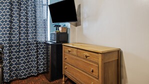 A room with a wooden dresser, a television mounted on the wall, and patterned curtains. - Fitzgerald Hotel (San Francisco)