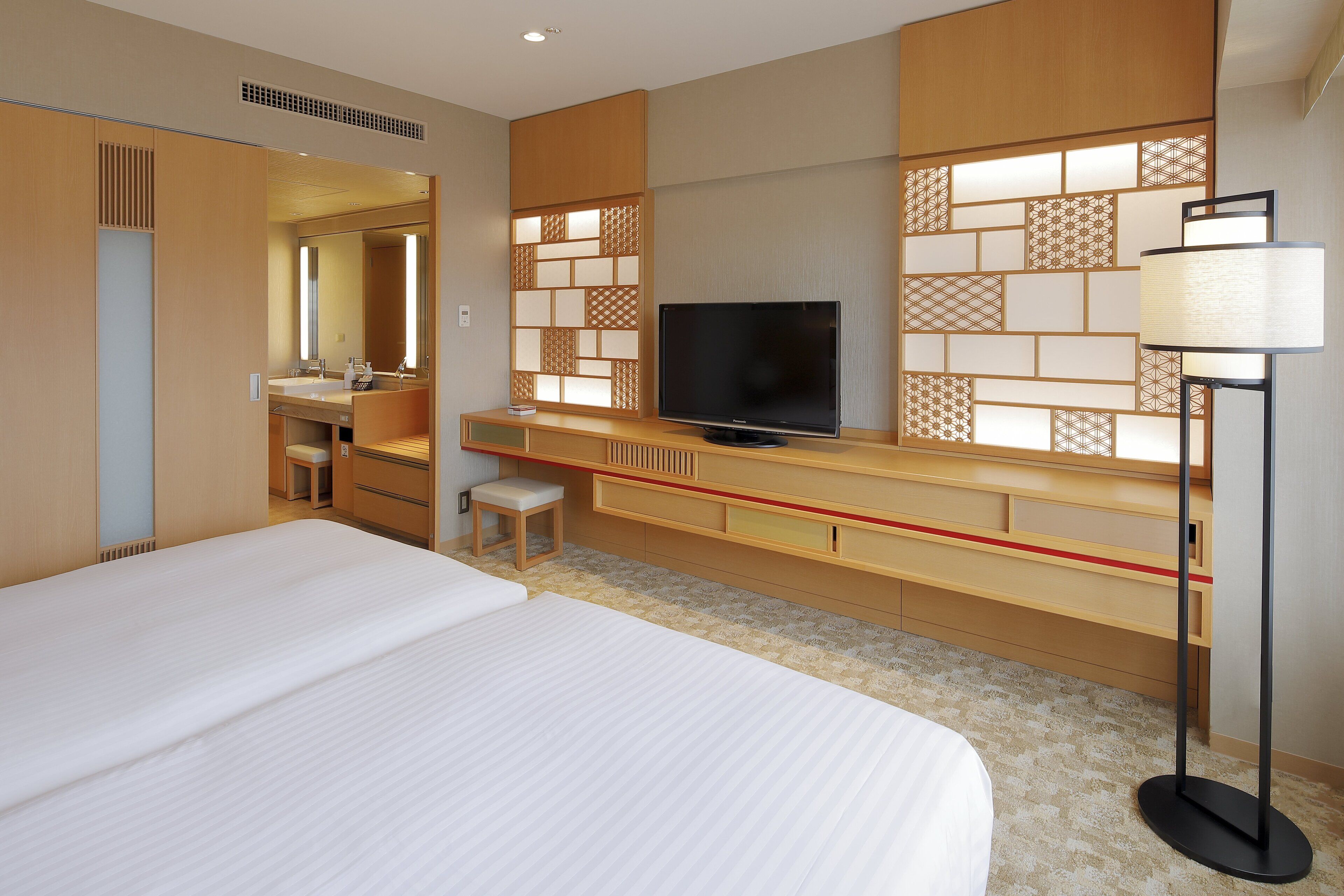 A hotel room with a large bed, a TV, a desk with a chair, and a mirror.
