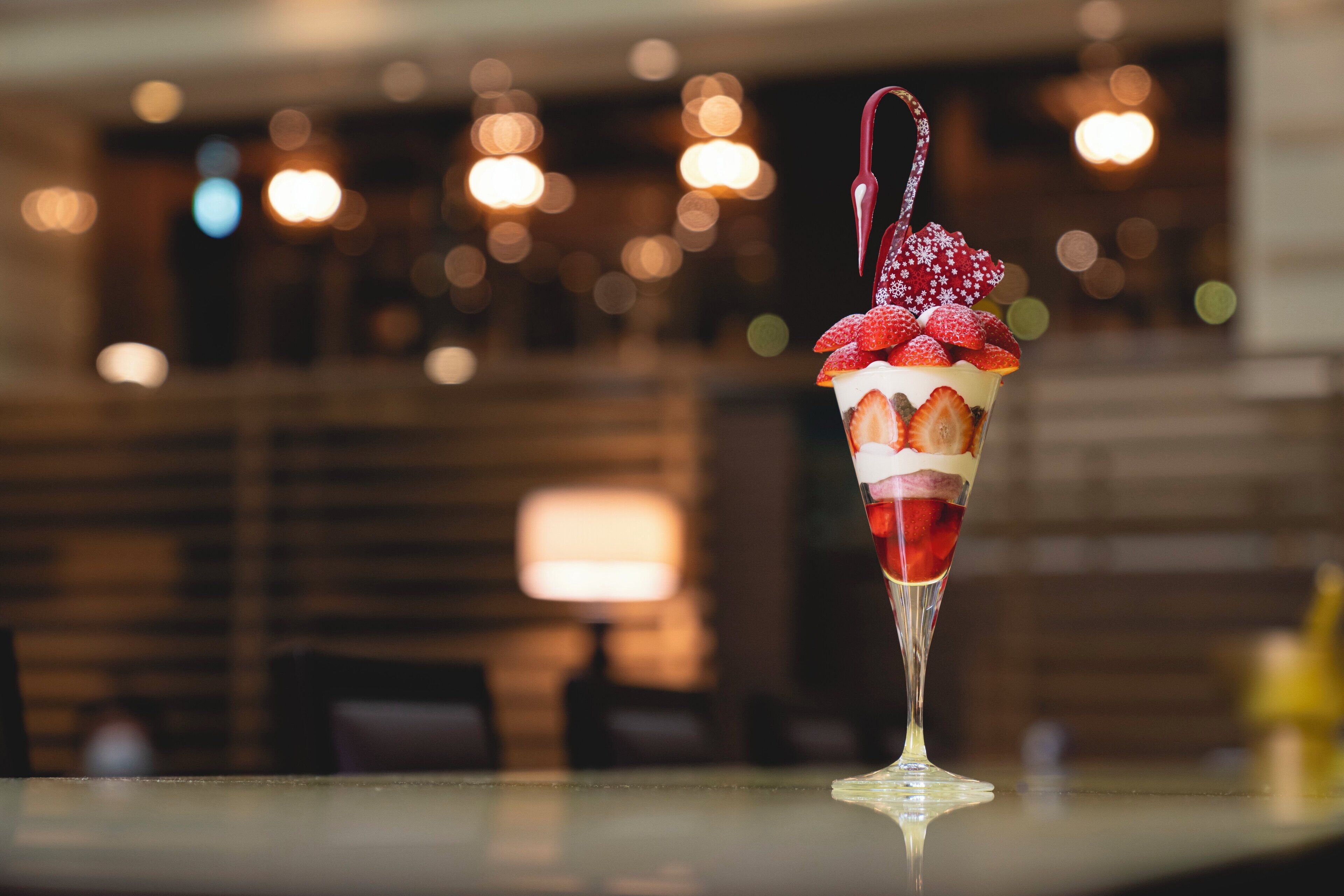Un postre en vaso sobre una mesa, con un fondo borroso de luces y una escalera.