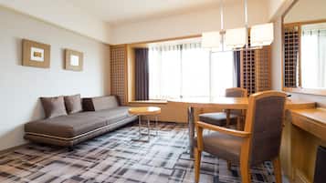 A modern living room with a sofa, dining table, chairs, and a large window with curtains.