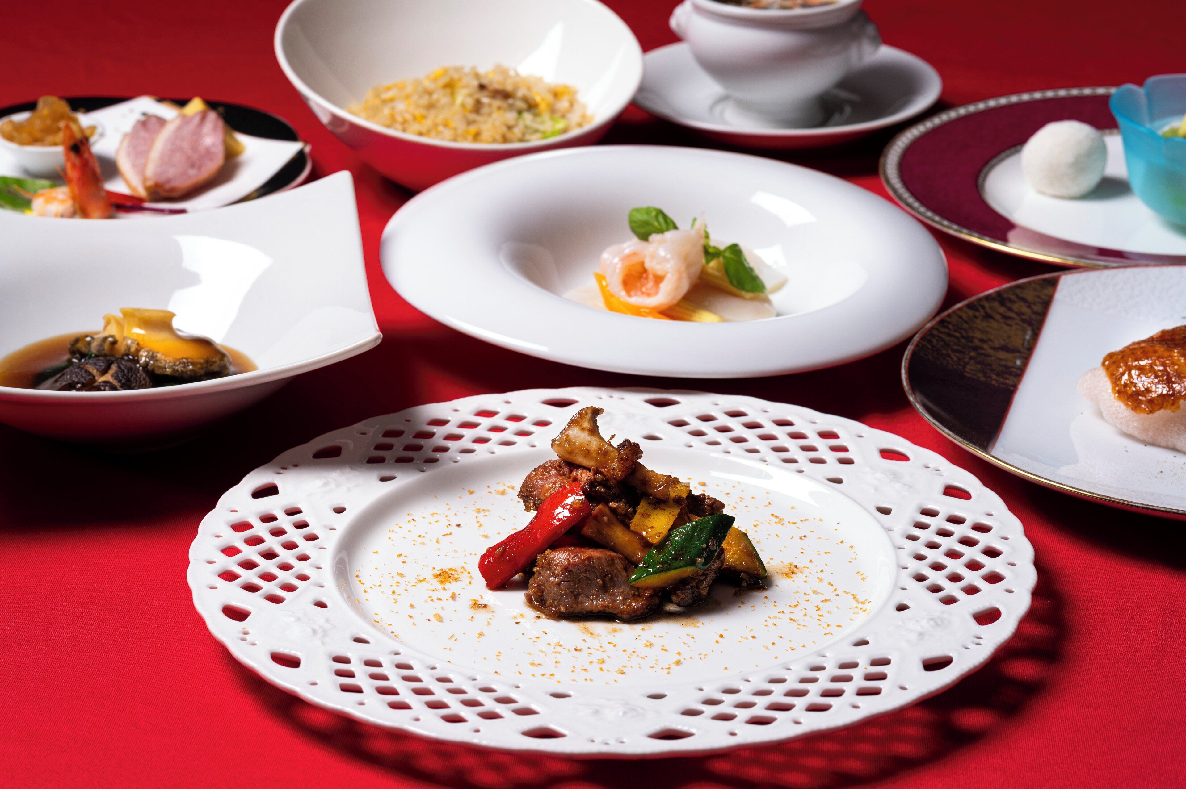 A variety of dishes on a table with a red tablecloth.