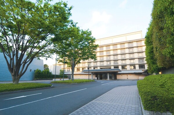 Stunning hotel entrance with a covered area and glass canopy, surrounded by lush greenery and a paved walkway.