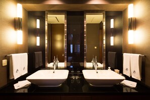 Bathroom features two sinks with a glossy countertop, wall-mounted lighting, and a textured pattern on the walls.