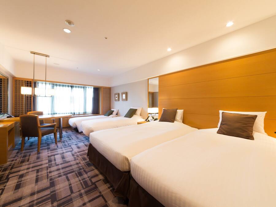Une chambre d’hôtel avec trois lits, un bureau et une chaise.