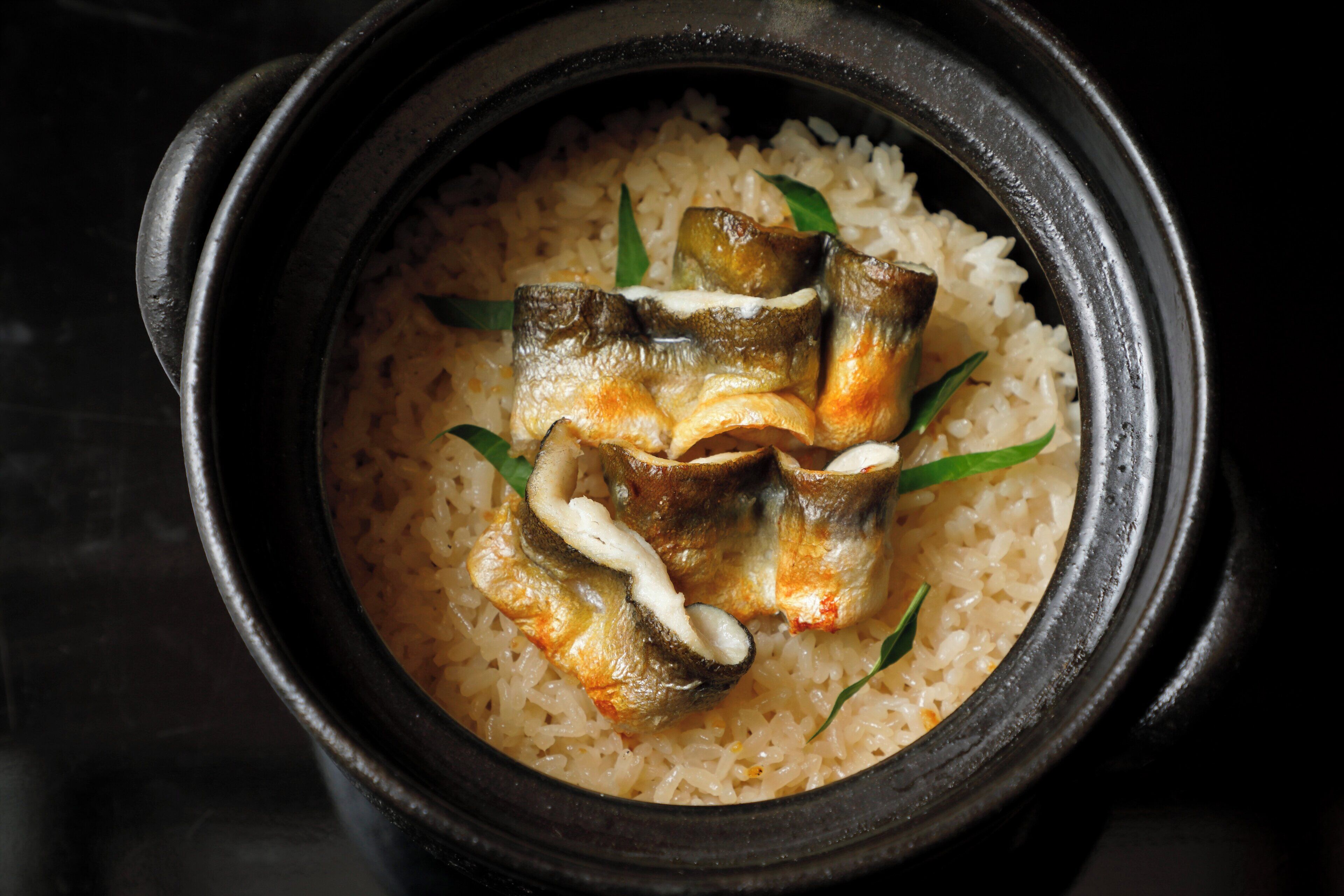 A pot of rice with fish and green leaves.